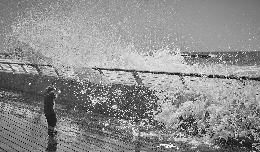 Back view of child standing against splashing sea waves