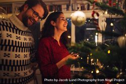 Man and woman smiling while decorating Christmas tree at home 0WZ2Ob