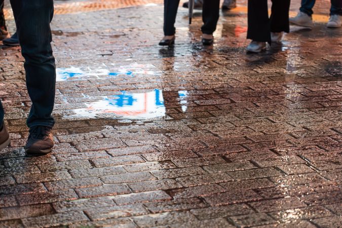 People walking on brick street in rainy evening with sign and lights are reflected in a water puddle