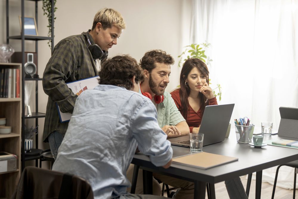 Young diverse creative team discussing project around laptop in bright co-working space