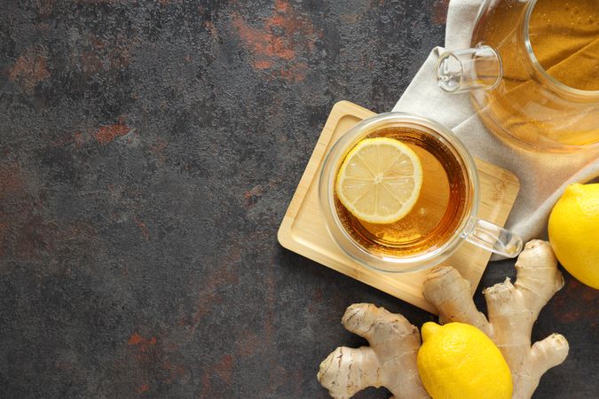 Cup and teapot with tea, lemon and ginger on gray background, space for text