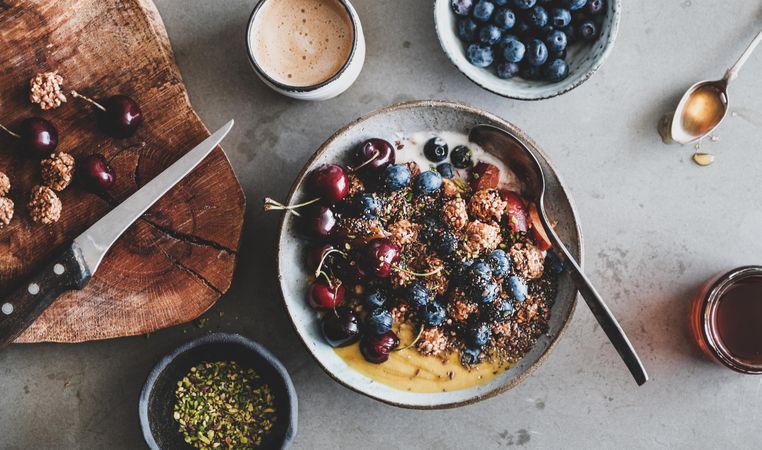 Oat granola yogurt bowl with cherries, blueberries, honey, nuts, coffee, wooden board