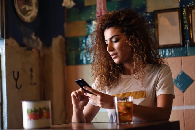 Arab woman in casual clothes checking her phone at restaurant table