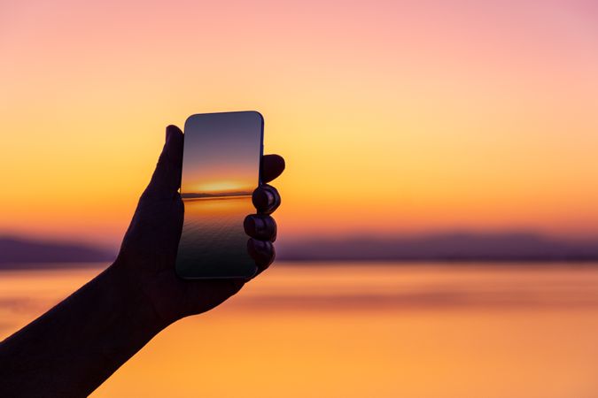 Crop traveler with photo of sunset on smartphone