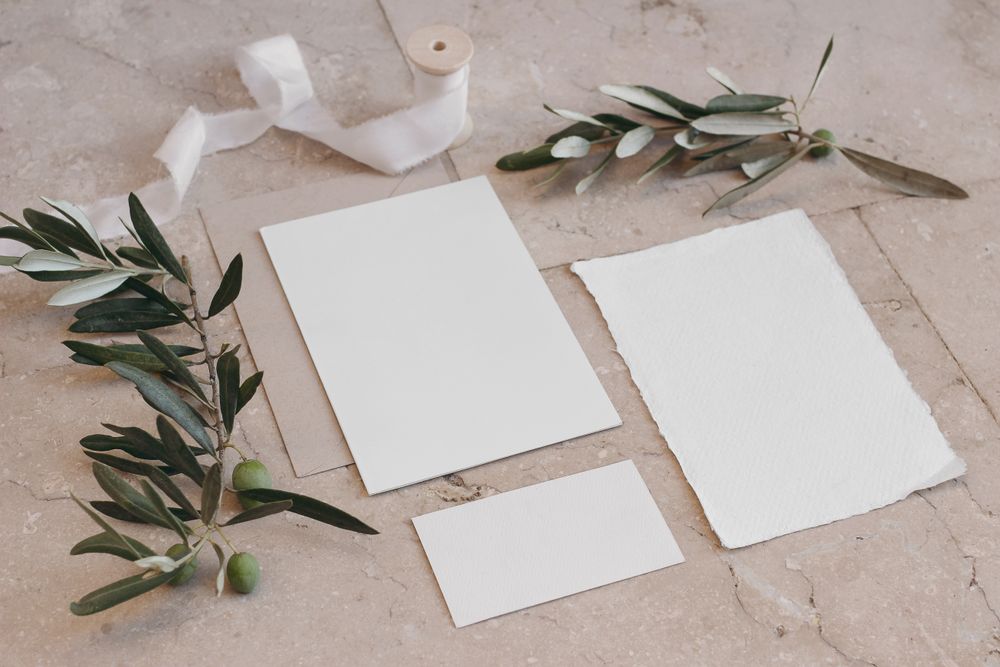 Three blank cotton paper cards on marble with dark green fig leaves & ribbon