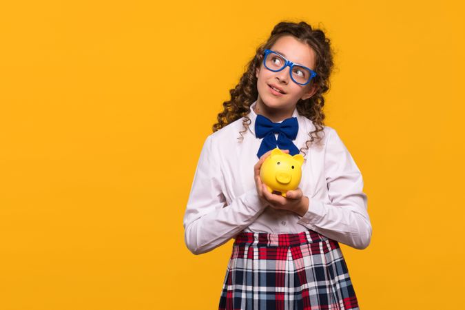 Girl holding yellow piggy bank thoughtfully.