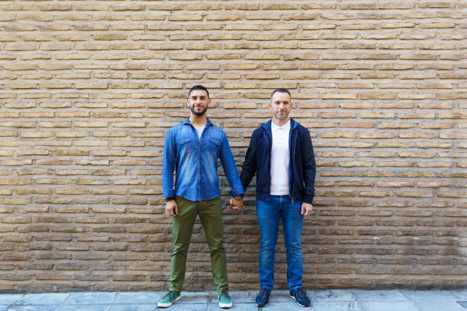 Gay couple holding hands posing in front of a brick wall