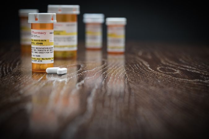 Variety of Non-Proprietary Prescription Medicine Bottles and Pills on Reflective Wooden Surface.