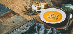 Pumpkin soup with croutons, seeds, spoon and bread on wooden table