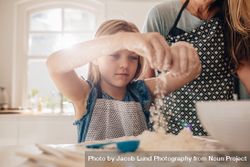 Girl making dough for baking with her mother standing by 4m9PB4