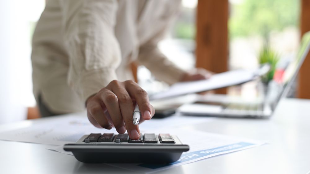 Close-up shot of Young man holding a pen and using a calculator placed in front