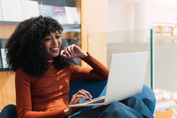 Smiling woman browsing laptop in library