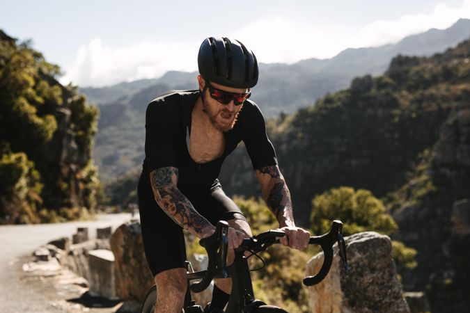Fit sportsman wearing helmet and sunglasses cycling outdoors up an inclined hill