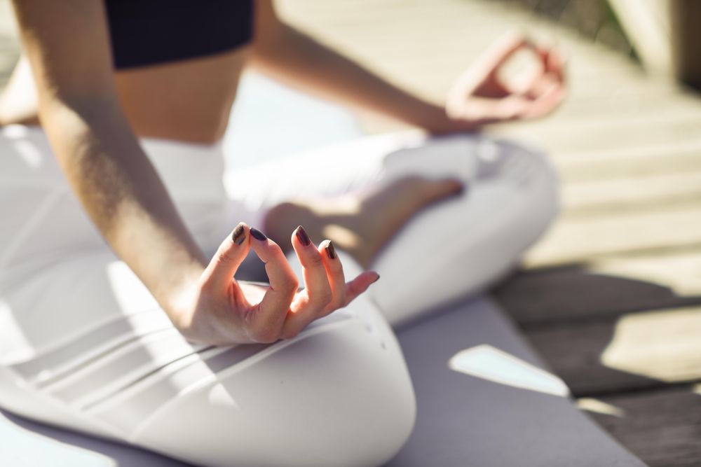 Close up of woman wearing sport clothes meditating on yoga mat on forest path