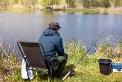 Fisherman with fishing rod on lake water background. Man catching fish by spinning on lakeside