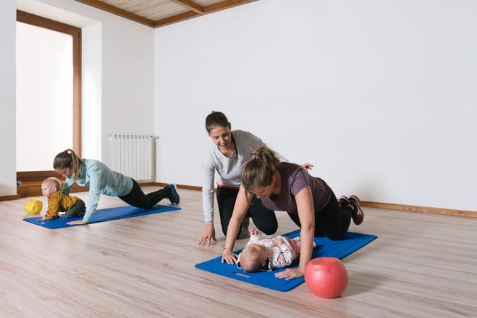 Fitness instructor helping mother with push ups