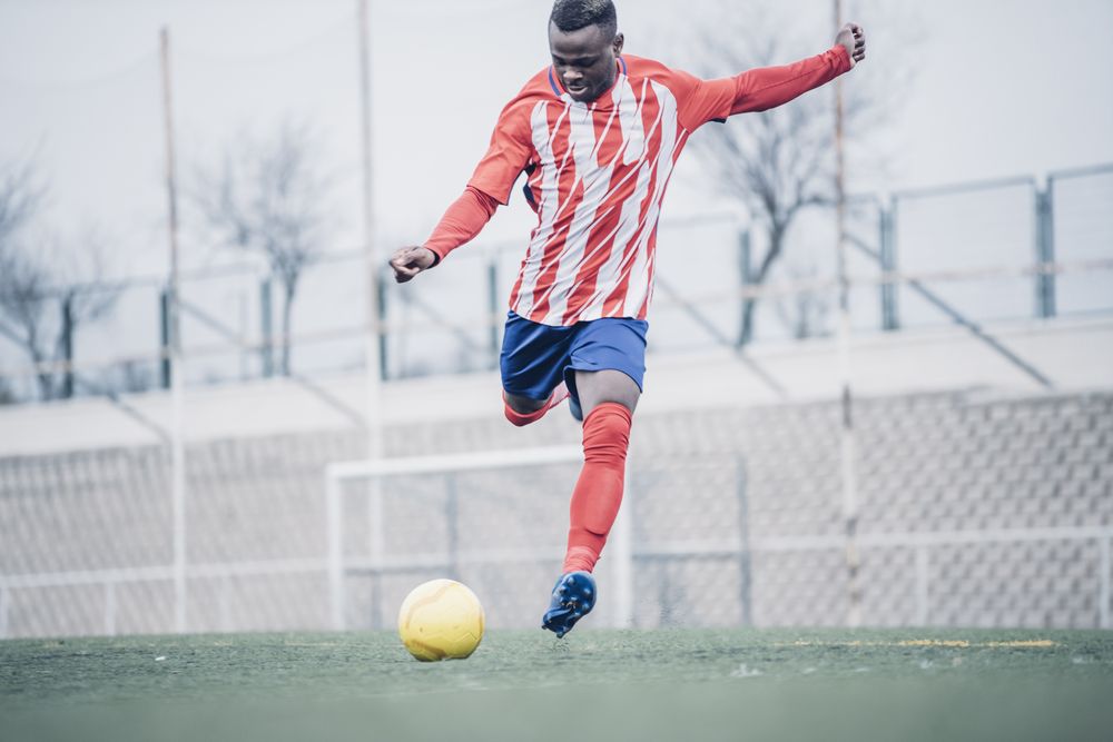 Black soccer player with red equipment playing soccer.