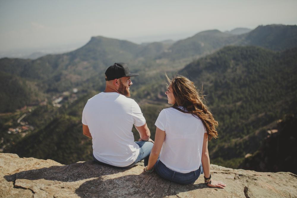 Happy couple talking while sitting at mountain cliff