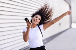 Arab woman in sport clothes with curly hair walking outside while dancing next to wall