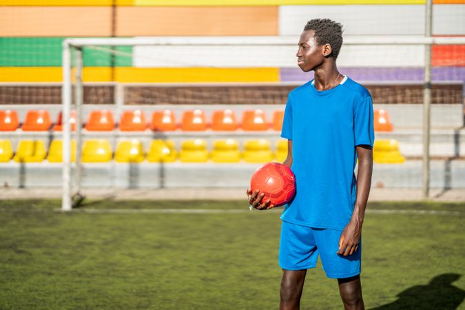 Black football player with ball standing on stadium