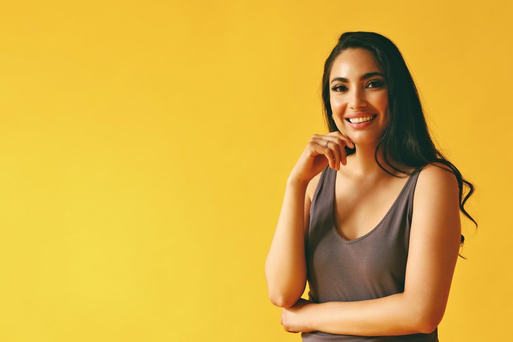 Confident happy Hispanic woman standing and looking at camera in yellow room, copy space