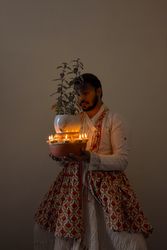 Indian man in kathak dress holding Tulsi Vivah plant surrounded with candles