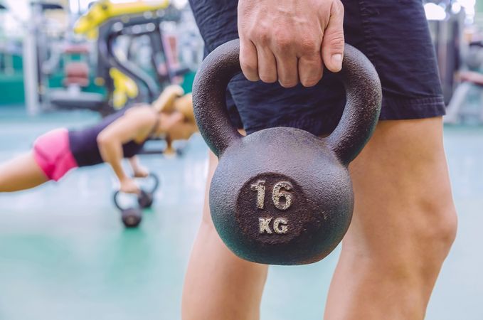 Man holding 16kg kettle bell in busy gym