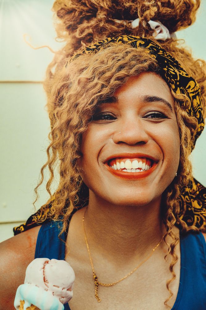 Vertical shot of happy Black female smiling with an ice cream cone in the sun