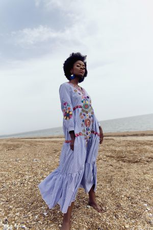 Woman in light dress with floral embroidery standing outdoor under blue sky