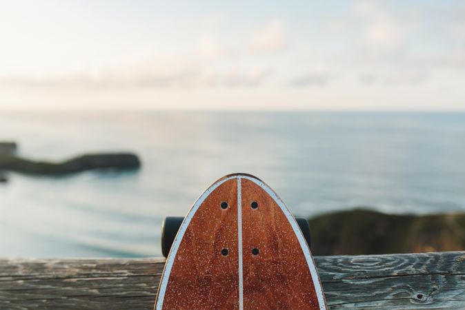 Surf skate leaning on wooden railing against blurred beach