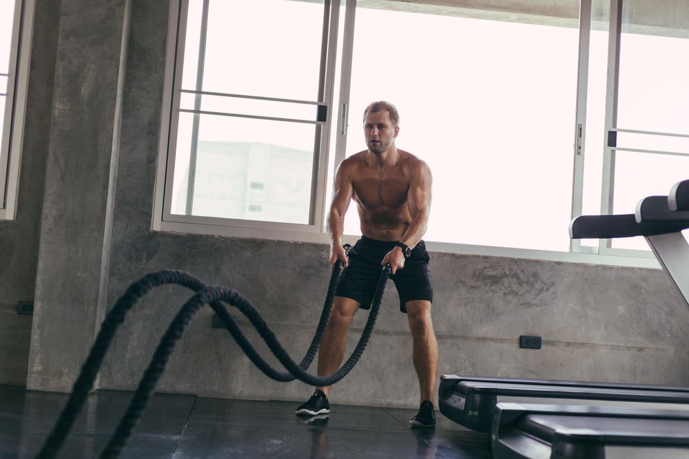 Intense athletic man training with rope in gym fitness