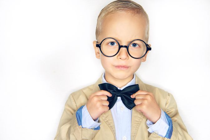 Serious blond boy in glasses fixing his bow tie