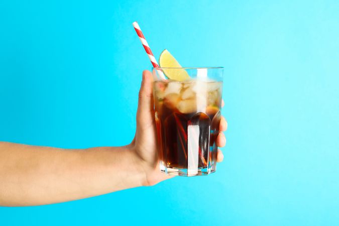 Female hand holding a glass with ice cola, tubule and lime slice