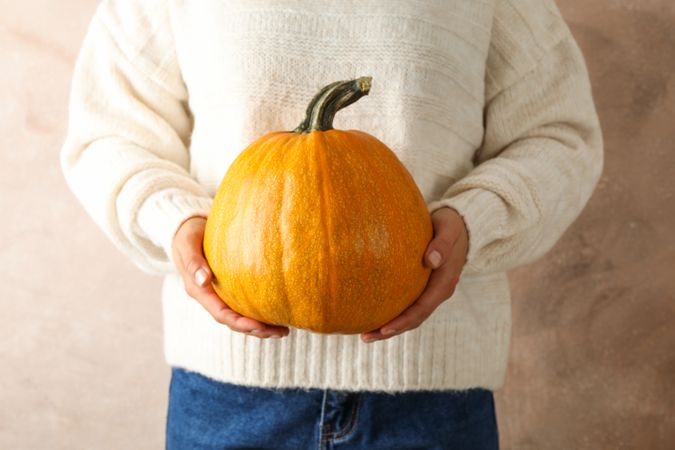 Young woman holding pumpkin on brown background, copy space
