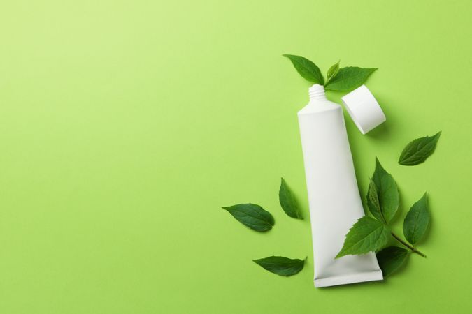 Toothpaste tube and mint leaves on green background, space for text