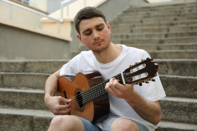 Young man sits on the steps and play on guitar