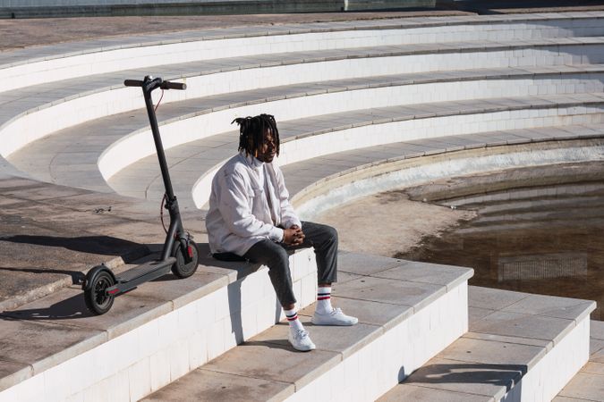 Black hipster man with scooter sitting on steps