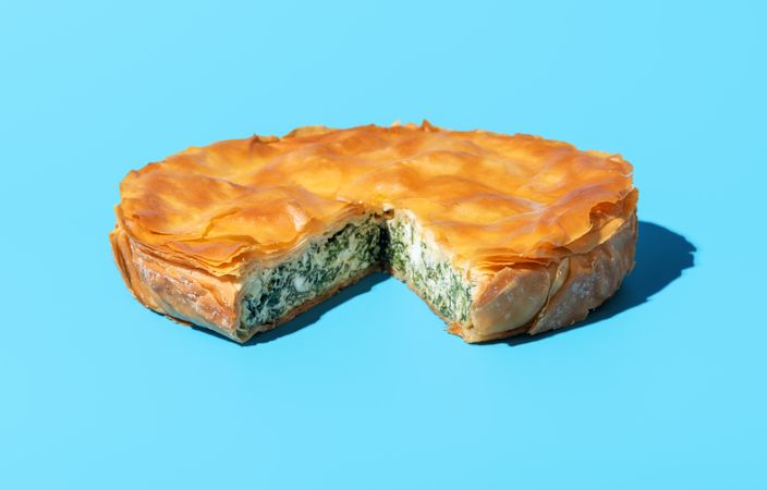 Phyllo cake with spinach and feta cheese, isolated on a blue background
