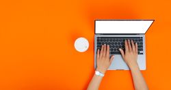 Banner of person using laptop on orange desk with take away cup of coffee or tea with copy space