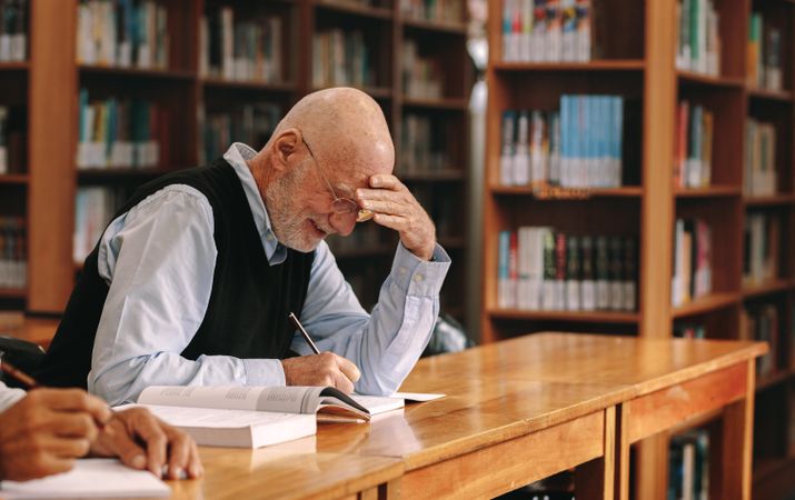 Smiling older man sitting in a library writing in a book