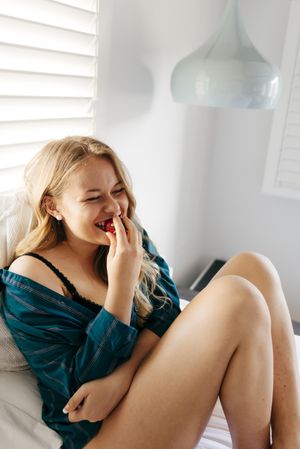 Young happy female holding strawberry bowl on bed