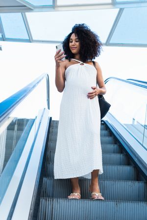 Pregnant Black woman browsing smartphone on escalator