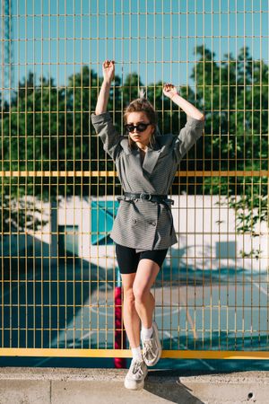 Stylish woman in sunglasses raising hands and leaning on lattice