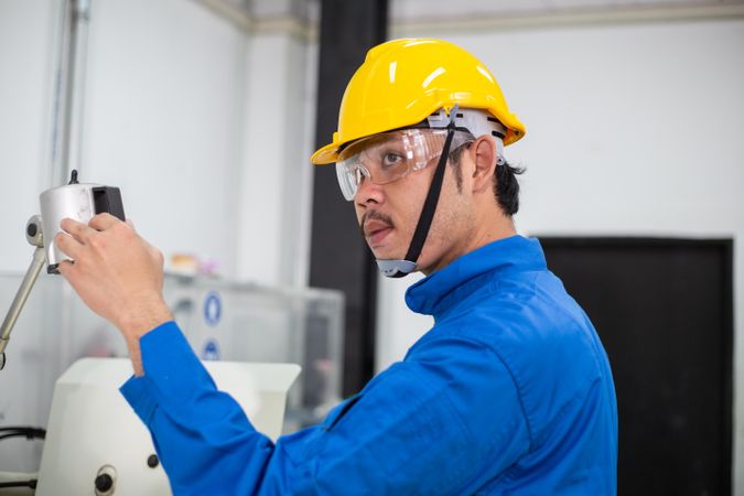 Asian man in blue jumpsuit and yellow hard hat working in manufacturing