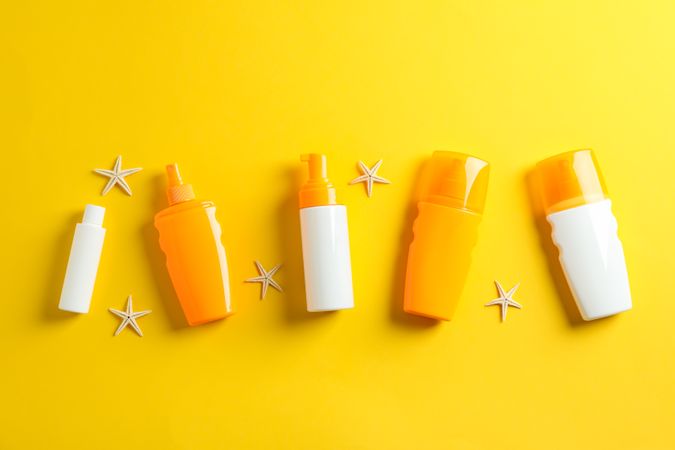 Flat lay composition with sunscreen sprays and starfishes on color background, space for text. Summer vacation backdrop