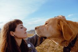 Woman with piercing sitting near dog between field