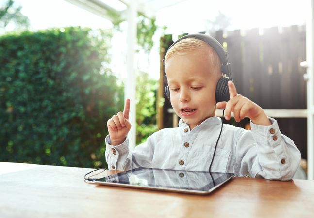 Blond boy using headphones and choosing music or show on digital tablet