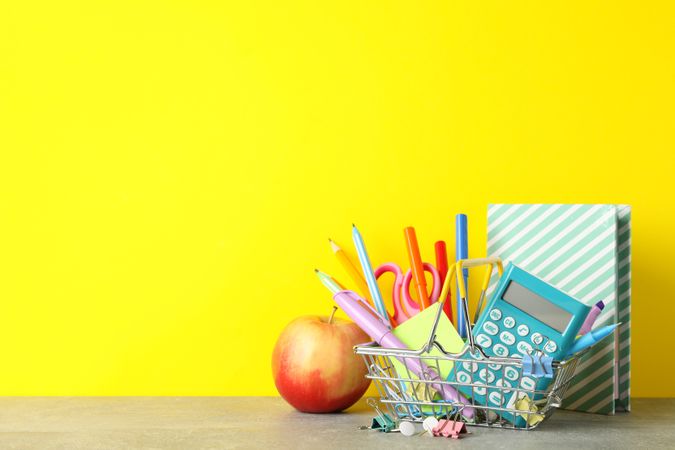 Basket of back to school supplies on desk with yellow wall