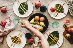 Fresh table setting with leaves on bright plates, fruit with person pouring from pitcher