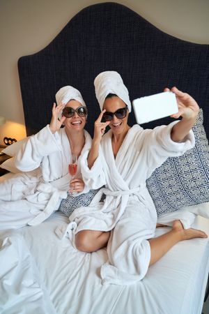 Cheerful women taking selfie on cellphone with glass of champagn